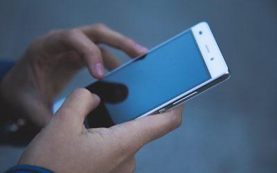 Des mains tiennent un smartphone avec l'écran allumé, doigts sur l'écran