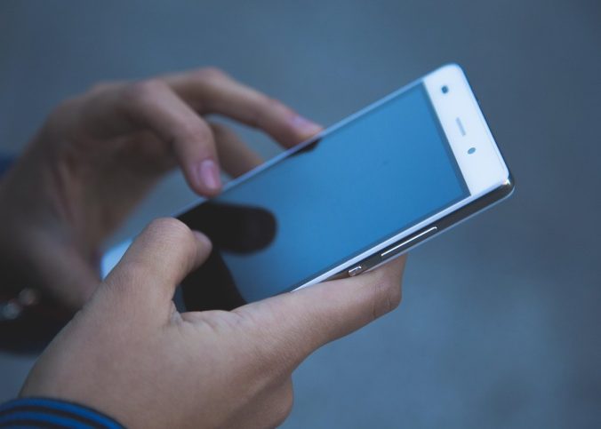 Des mains tiennent un smartphone avec l'écran allumé, doigts sur l'écran