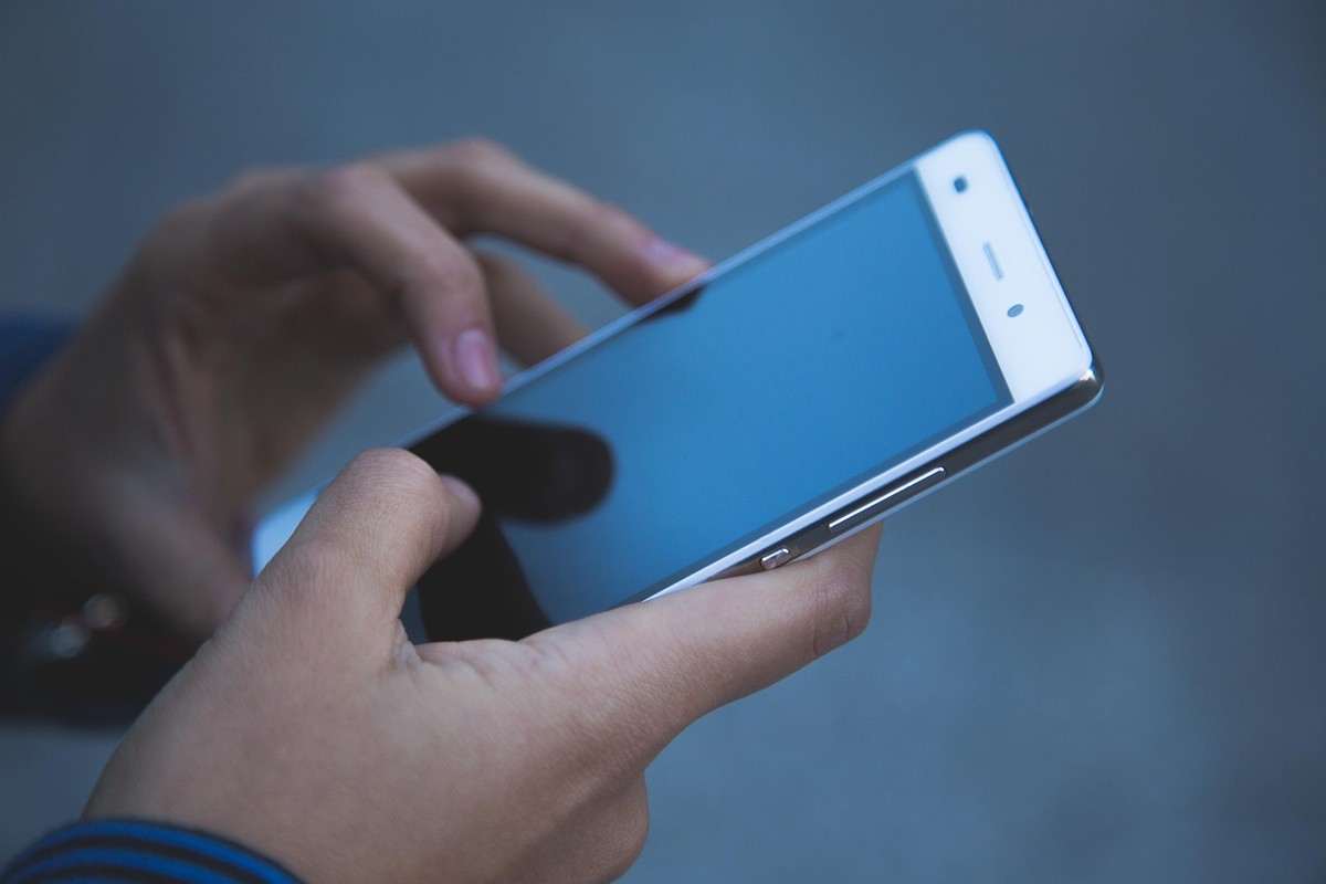 Des mains tiennent un smartphone avec l'écran allumé, doigts sur l'écran