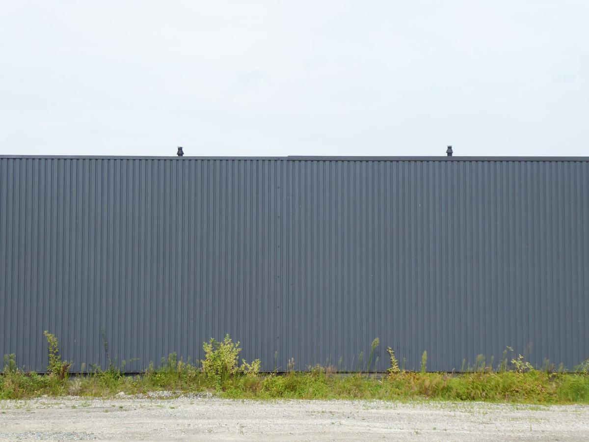 Un mur métallique gris sous un ciel clair, herbe et gravier au sol Un mur métallique gris sous un ciel clair, herbe et gravier au sol