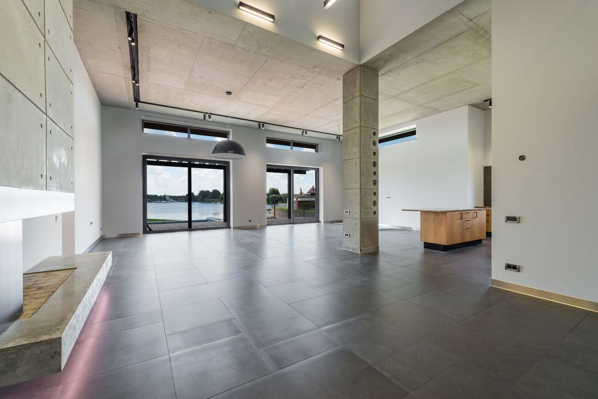Intérieur vaste de style loft avec colonne béton, baies vitrées sur paysage, sol carrelé gris Intérieur vaste de style loft avec colonne béton, baies vitrées sur paysage, sol carrelé gris
